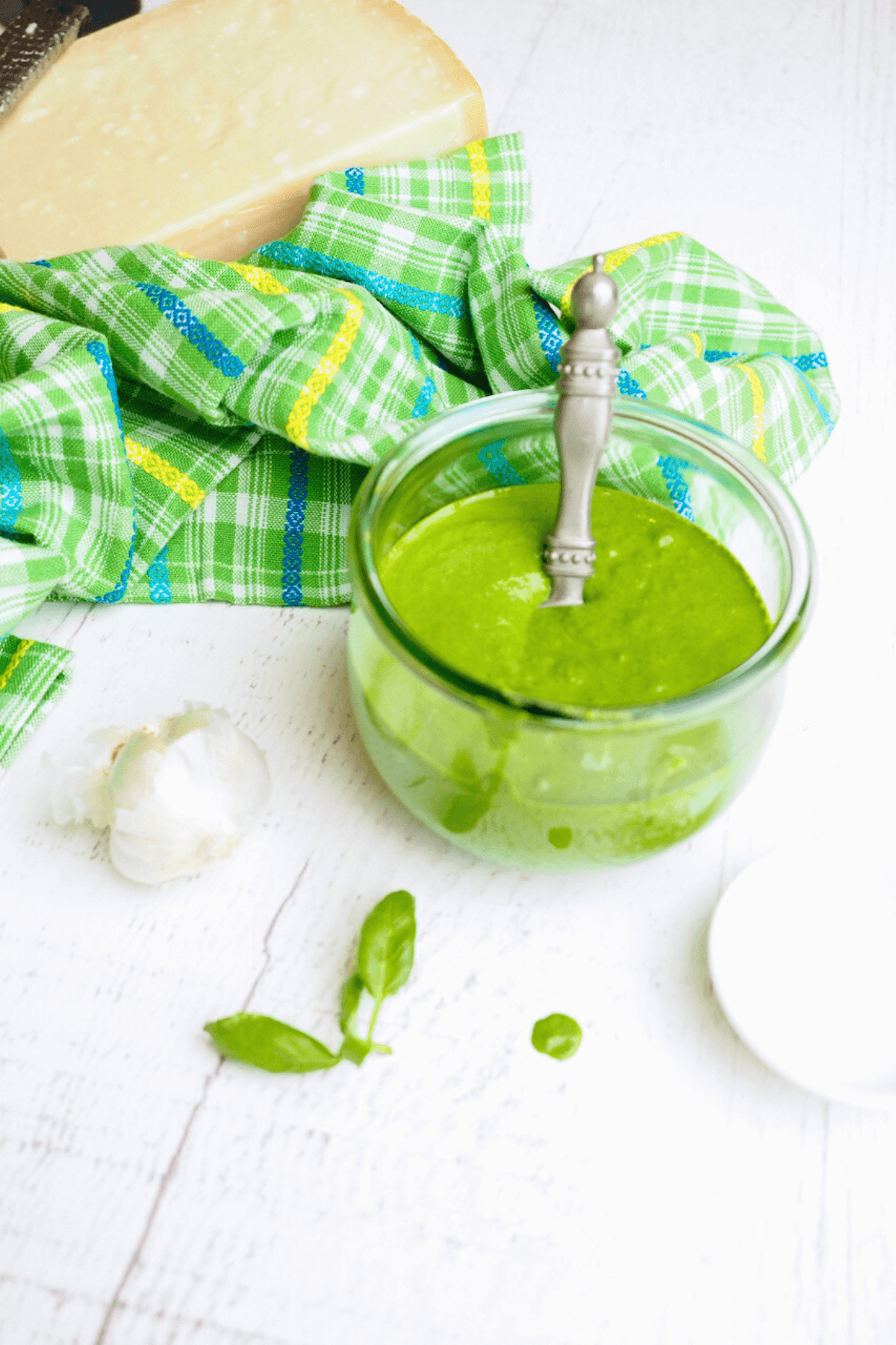 How to make pesto without nuts with jar of pesto sauce filled with scoop inside, some garlic and fresh basil nearby.