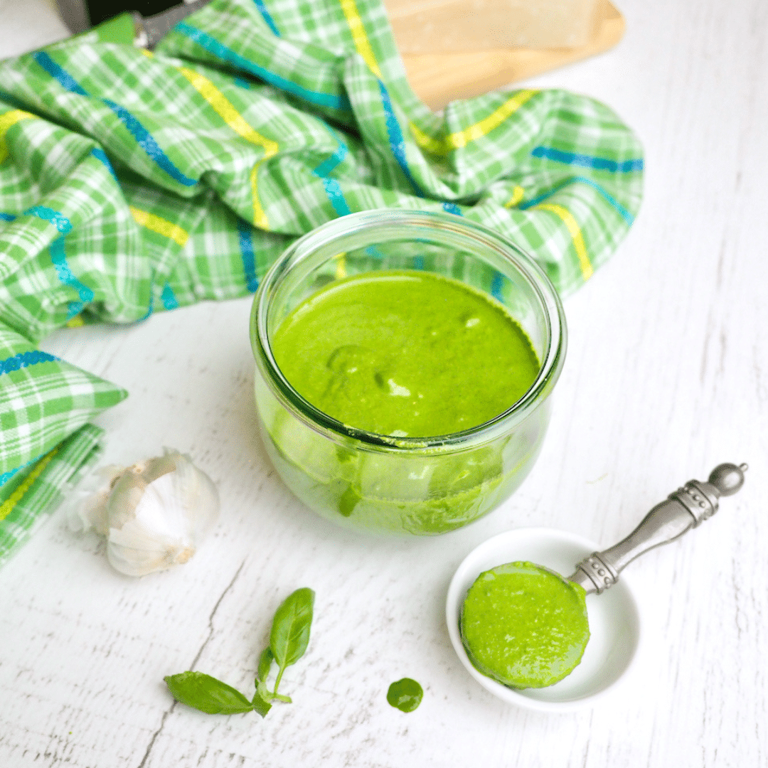 square image of spinach basil pesto that is nut free in pretty glass jar with spoonful removed.. 