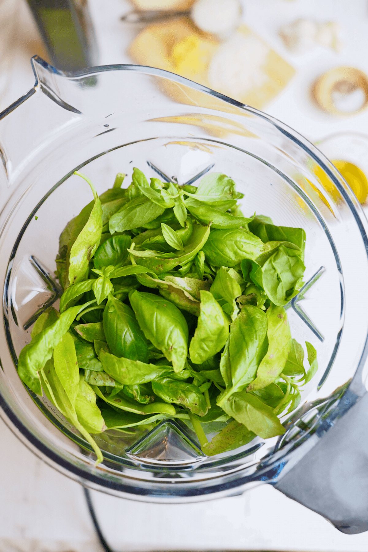 Fresh spinach and basil in hopper of high speed blender for spinach basil pesto without nuts.