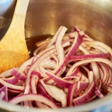 Sliced red onions in saucepan with brine and wooden spoon.