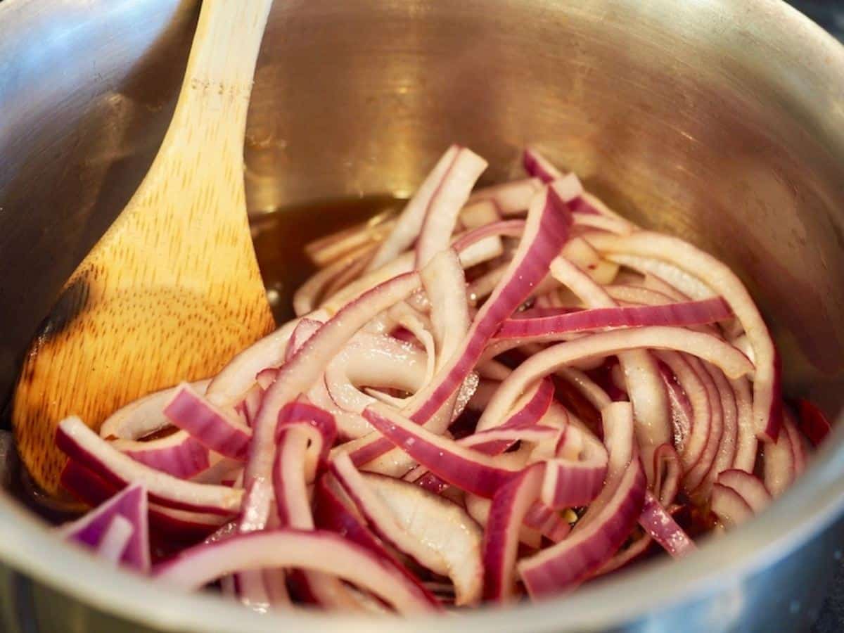 Sliced red onions in saucepan with brine and wooden spoon.