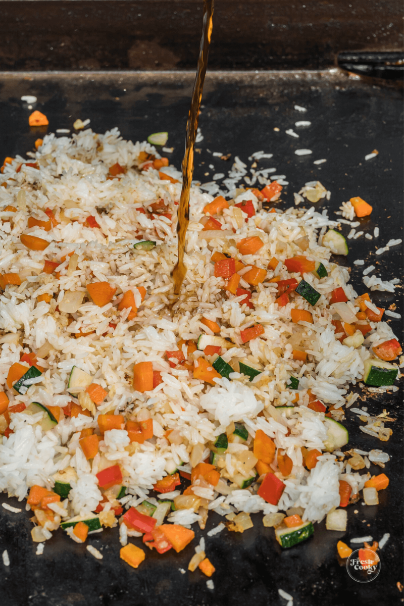 Adding sauces to fried rice and veggies on griddle. 