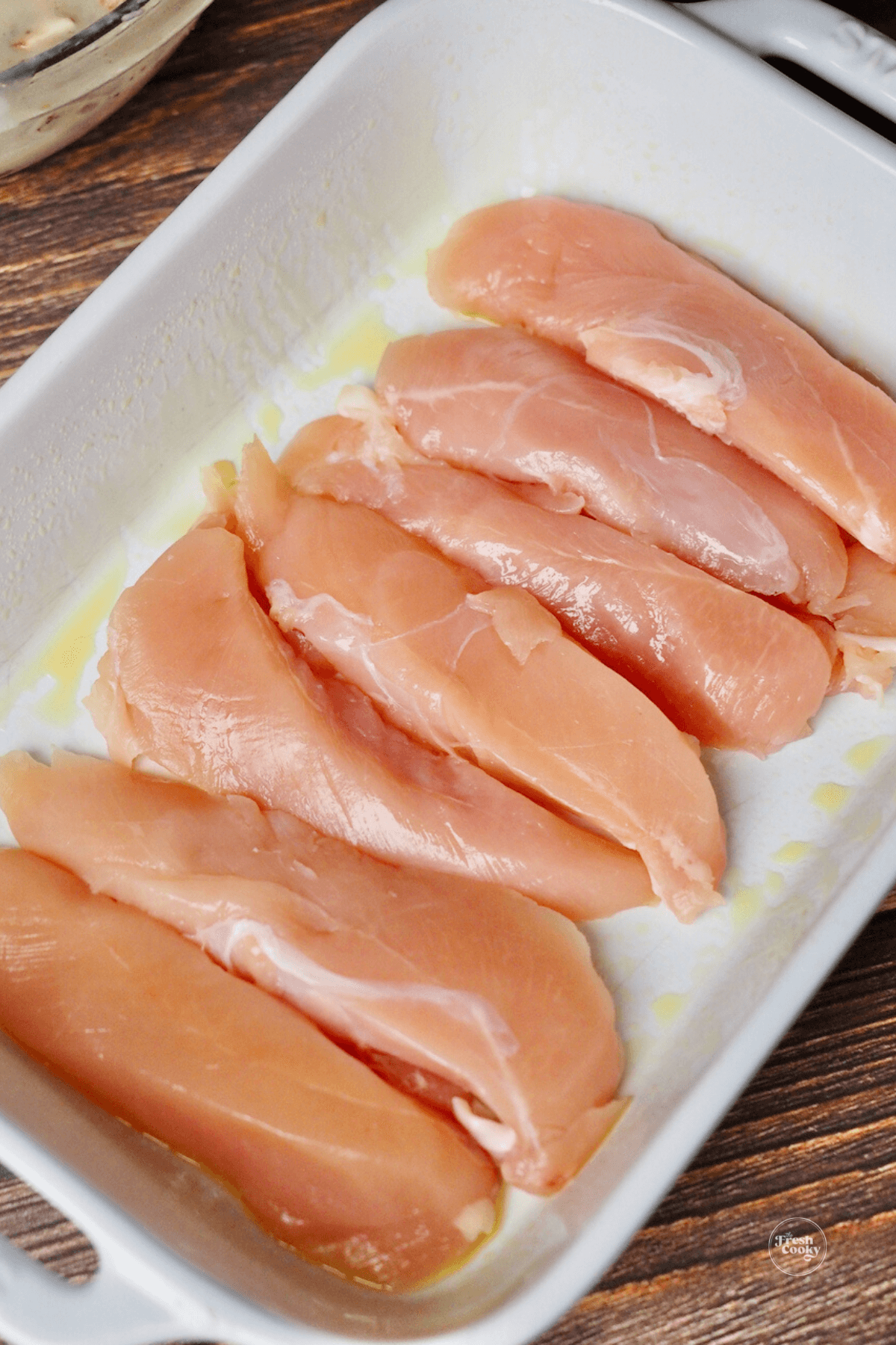 Chicken tenderloins layered evenly on bottom of white casserole dish.