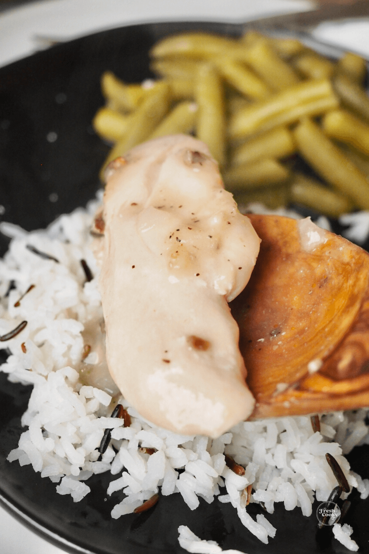 Wooden spoon with chicken tenderloin spooning onto rice.