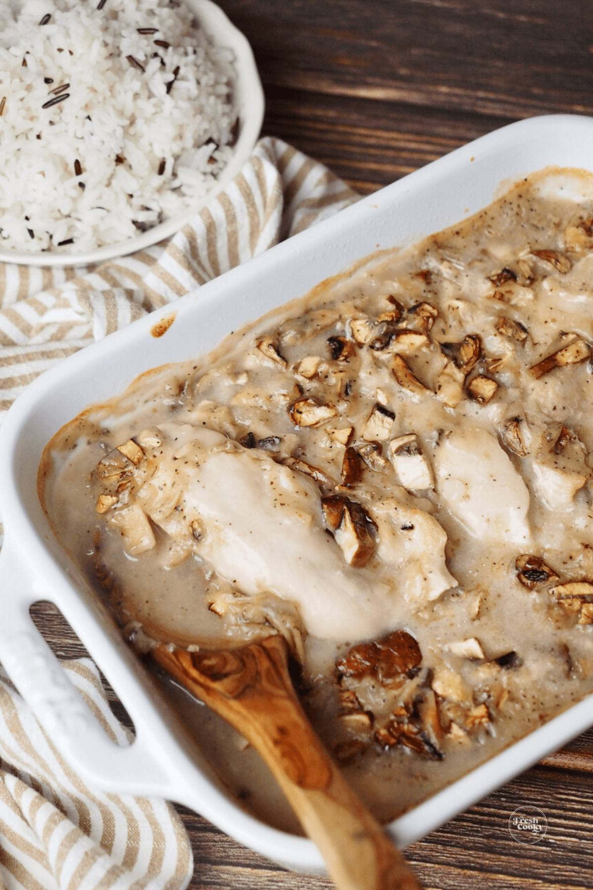 Casserole dish filled with creamy Copycat Cracker Barrel Chicken and Rice recipe with wooden spoon.