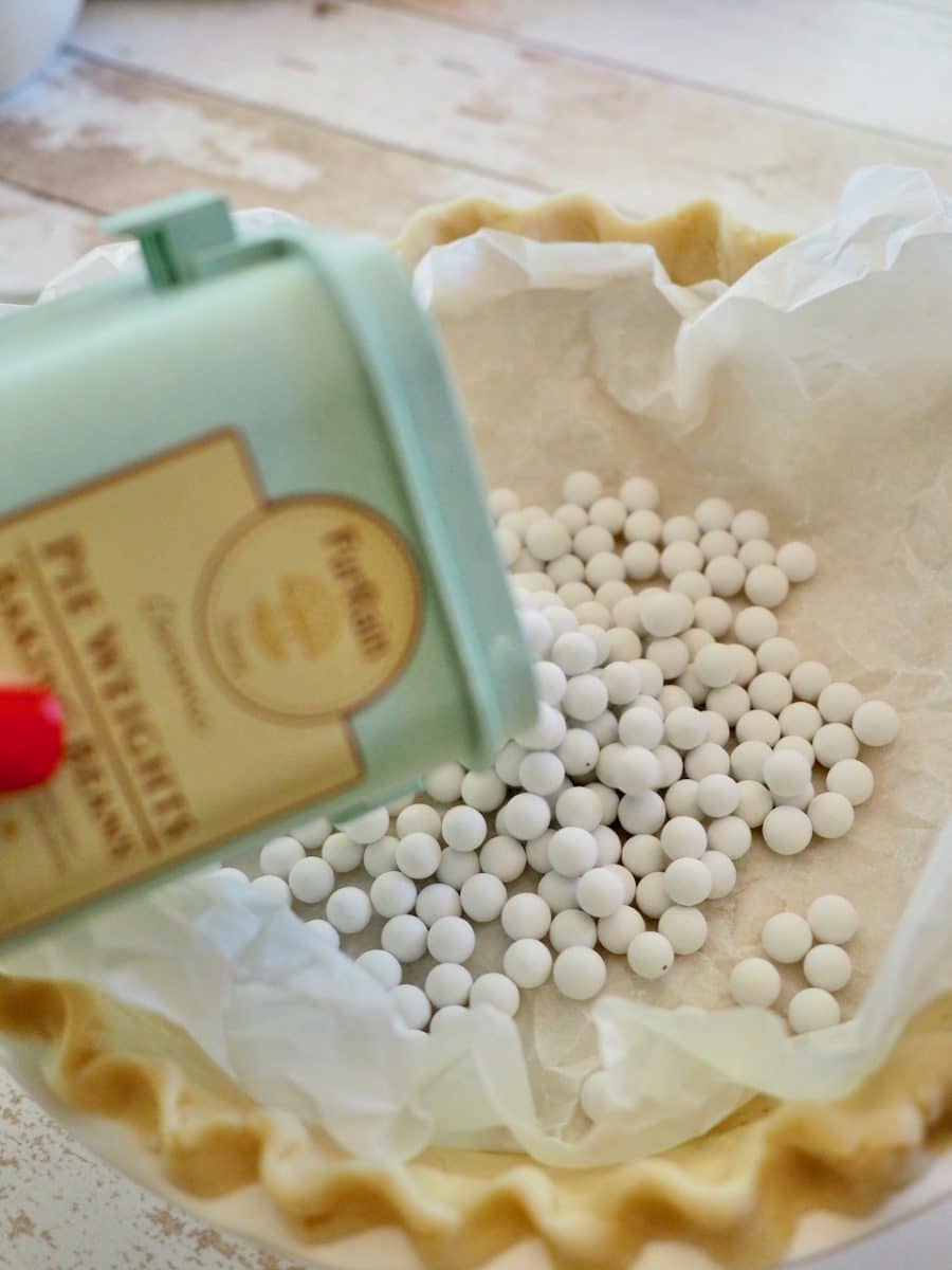 Pouring pie weights into unbaked pie shell.