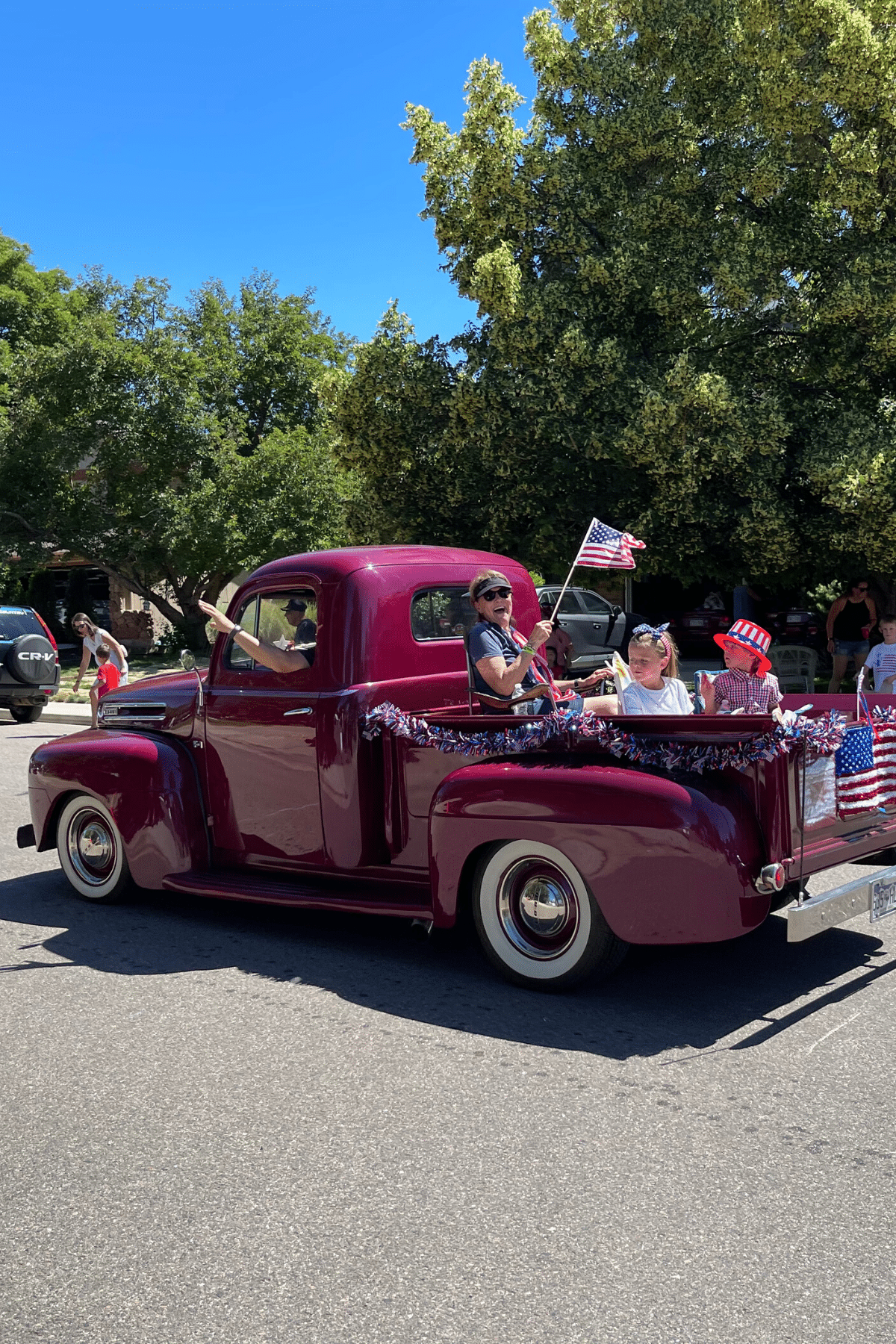 Classic old pick up truck decorated for 4th of  July with people sitting in back waving American flag. 