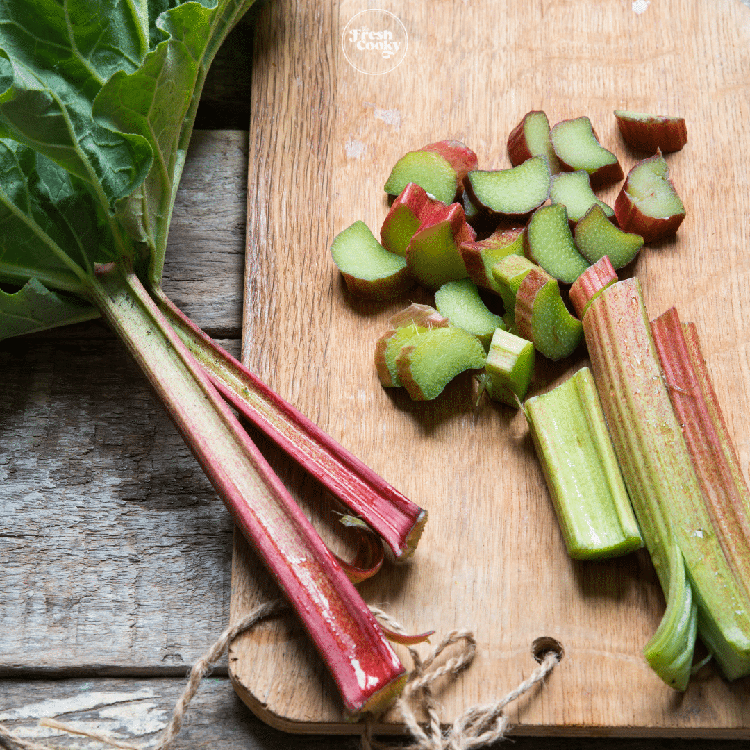 stalks of rhubarb with leaves on a cutting board, with diced rhubarb.