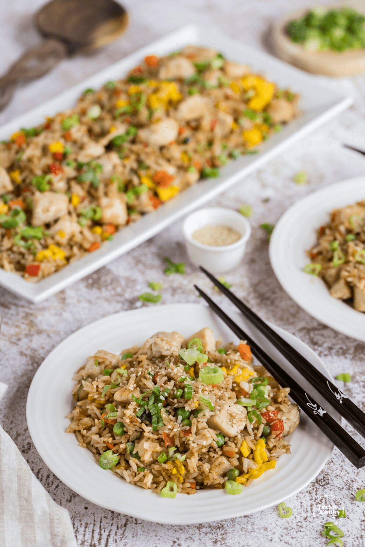 Chicken Fried Rice made on a blackstone griddle on table in serving tray, with two plates full of rice with chopsticks resting on the side of the dish.
