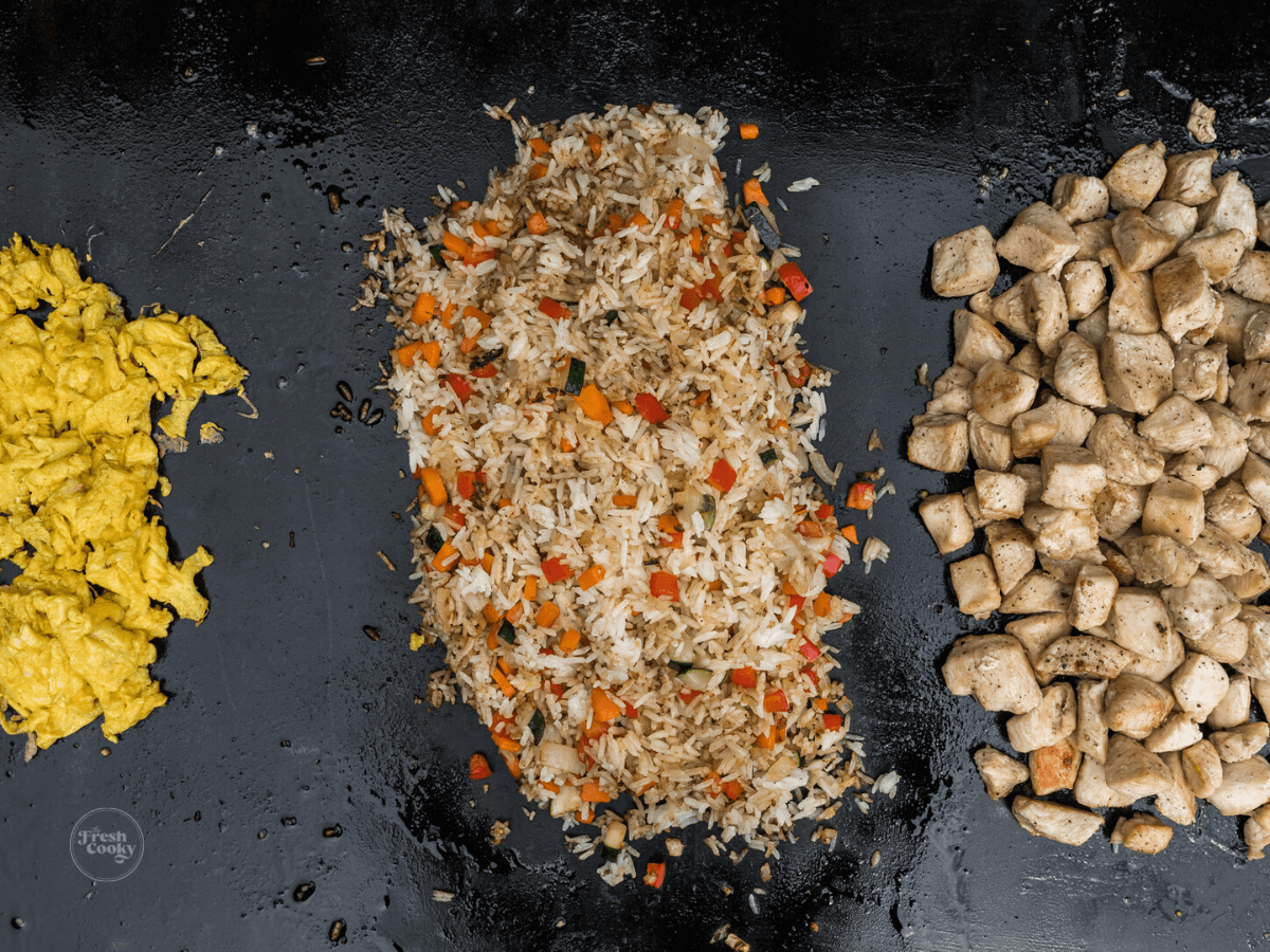 Chicken, Veggies and rice and scrambled eggs separated on blackstone griddle.