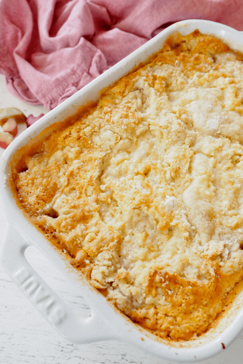 Baked rhubarb dump cake in staub white baking dish with pink napkin behind.