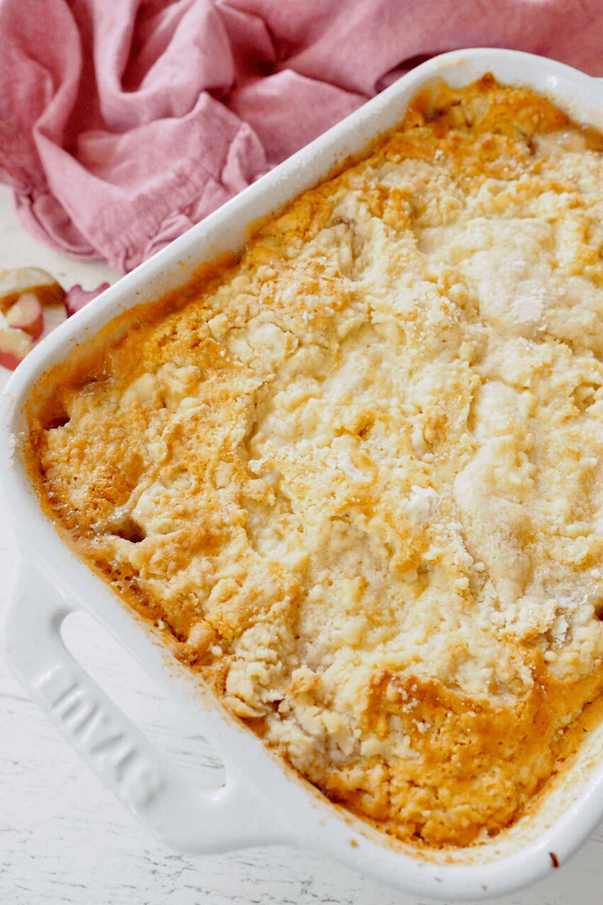 Baked rhubarb dump cake in staub white baking dish with pink napkin behind.