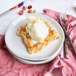 slice of rhubarb dump cake with scoop of vanilla ice cream, forks on side with pink napkin.