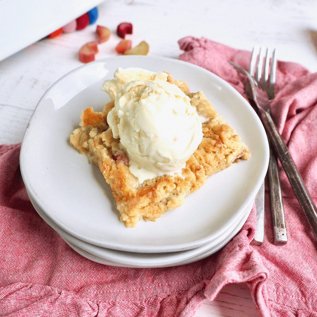 slice of rhubarb dump cake with scoop of vanilla ice cream, forks on side with pink napkin.