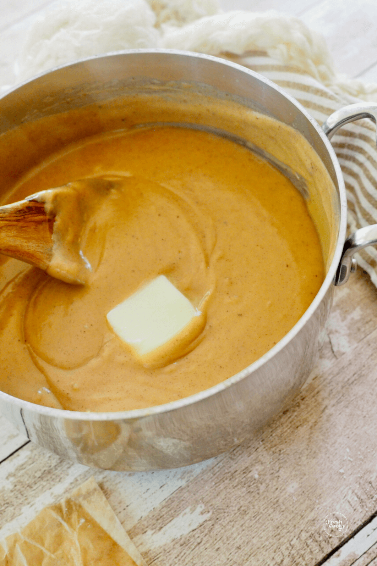 Wooden spoon stirring butter into butterscotch pudding in heavy bottomed pan.