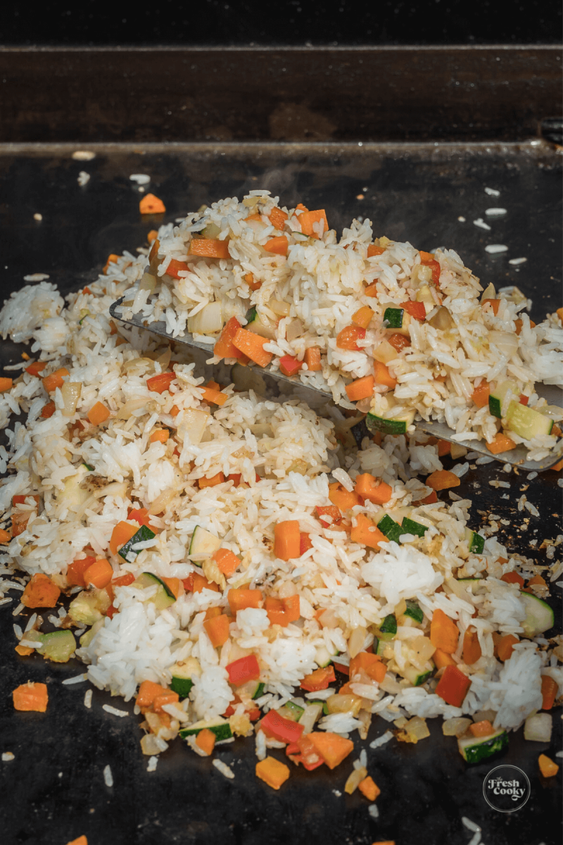 Adding rice to chicken and veggies on Blackstone griddle.