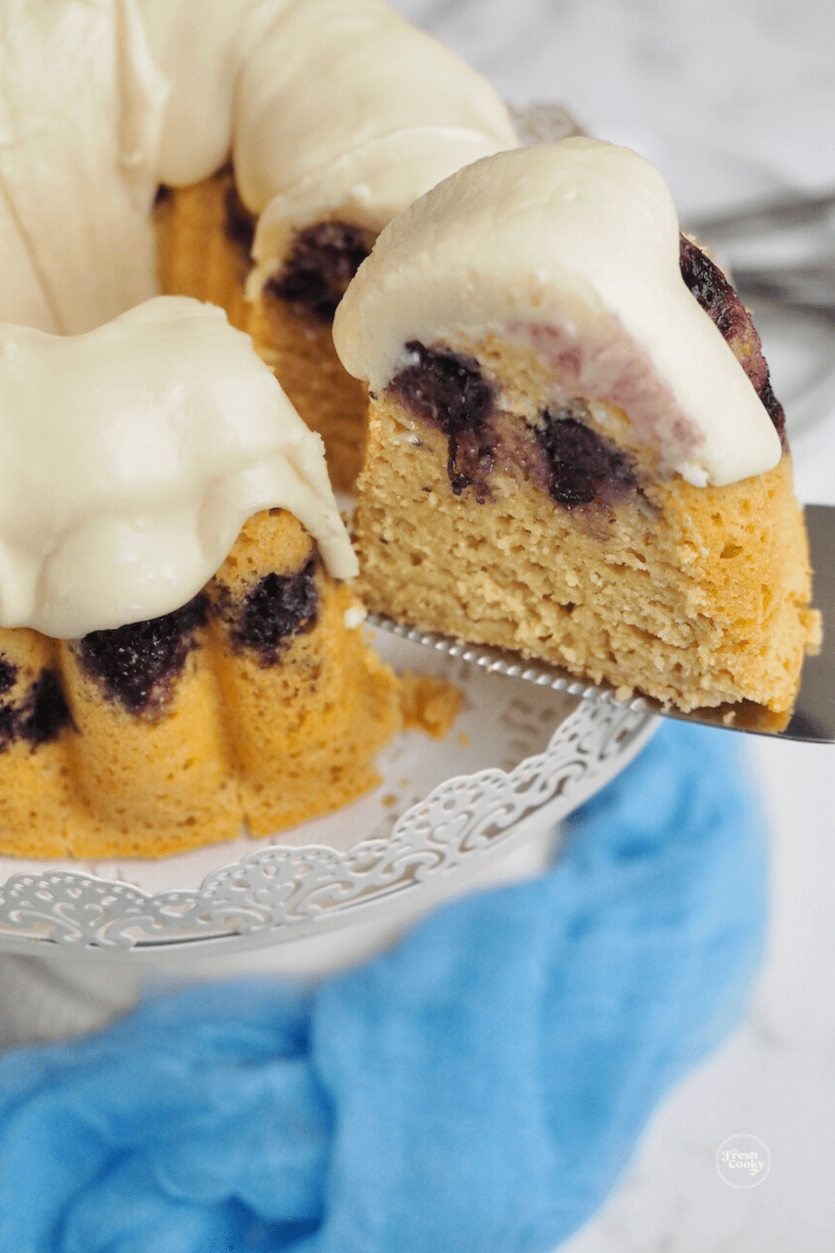 Removing a slice of blueberry pancake bundt cake from pedestal.