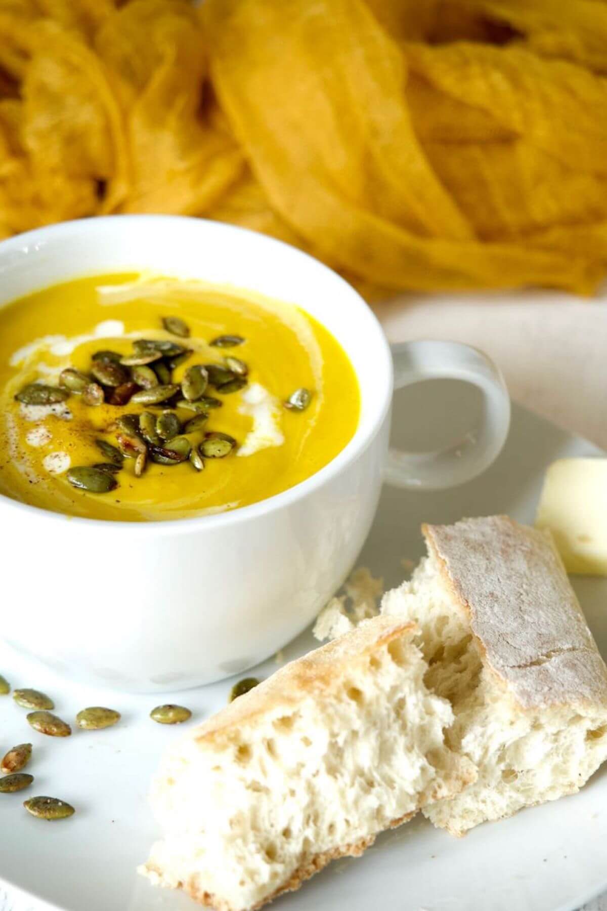 Easy copycat Panera autumn squash soup in white soup bowl served with fresh French bread and butter.