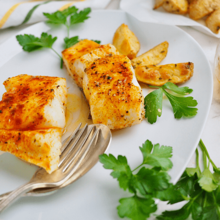 Cooked halibut filets on plate seasoned with red paprika and garnished with parsley.