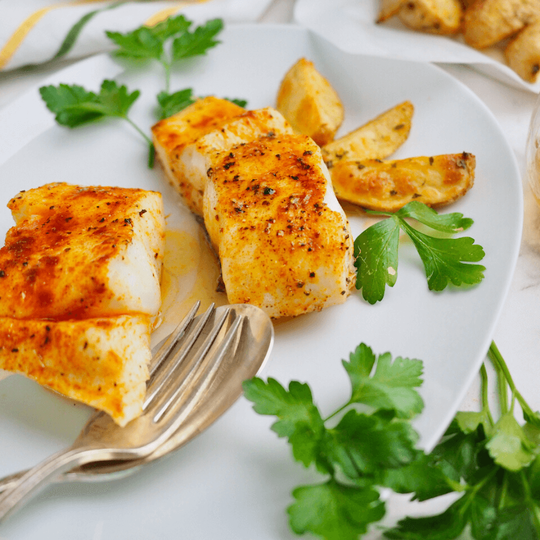 Cooked halibut filets on plate seasoned with red paprika and garnished with parsley.