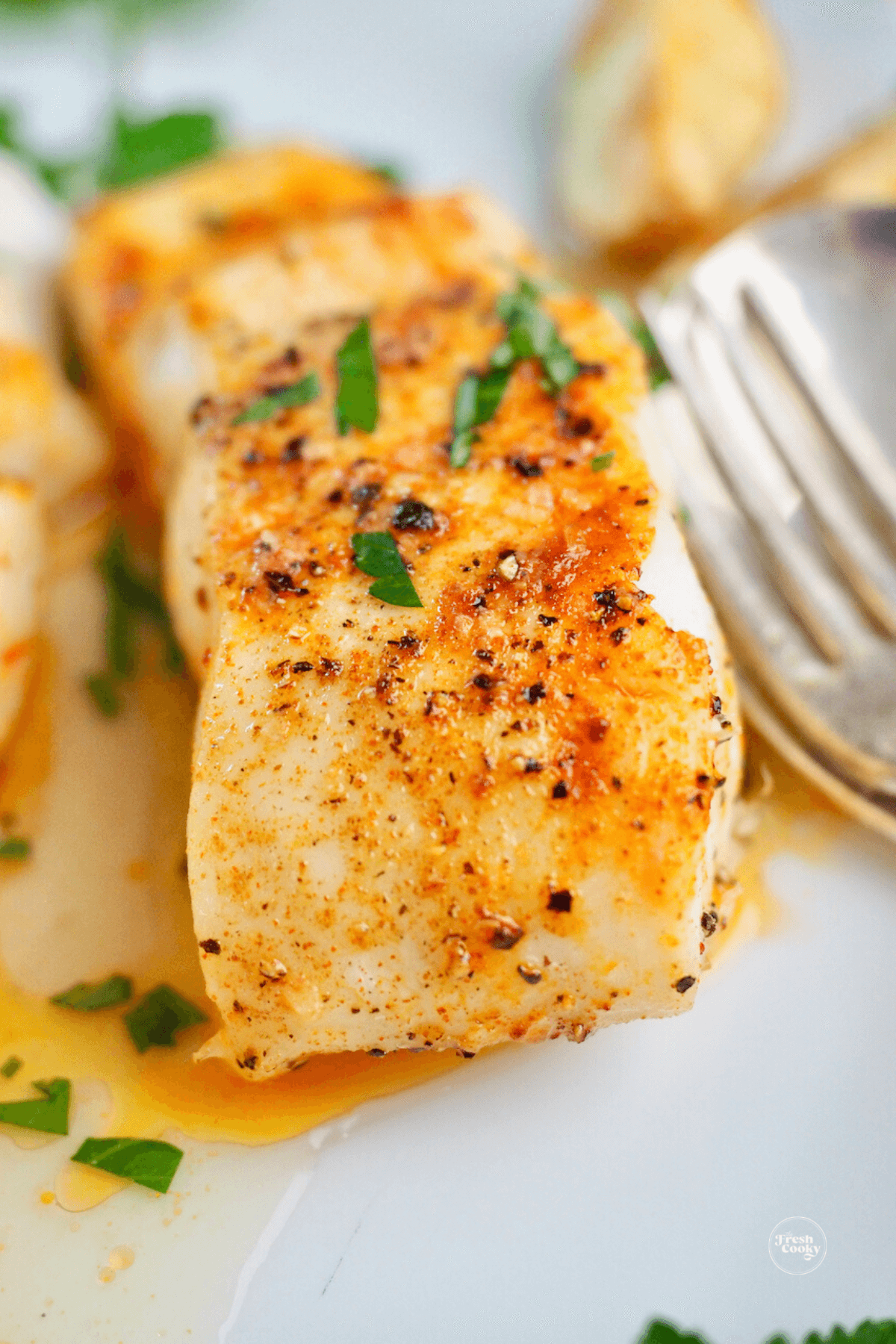 Close up of flaky cooked halibut on plate.