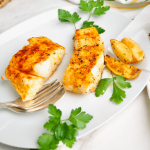 Two halibut filets cooked on white plate with steak fries and garnished with parsley.