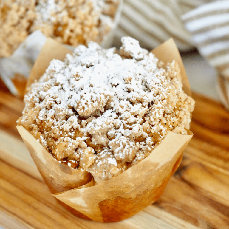 Panera Pumpkin Muffin Recipe with muffin parchment paper liner on board sprinkled with powdered sugar on the crumb topping.