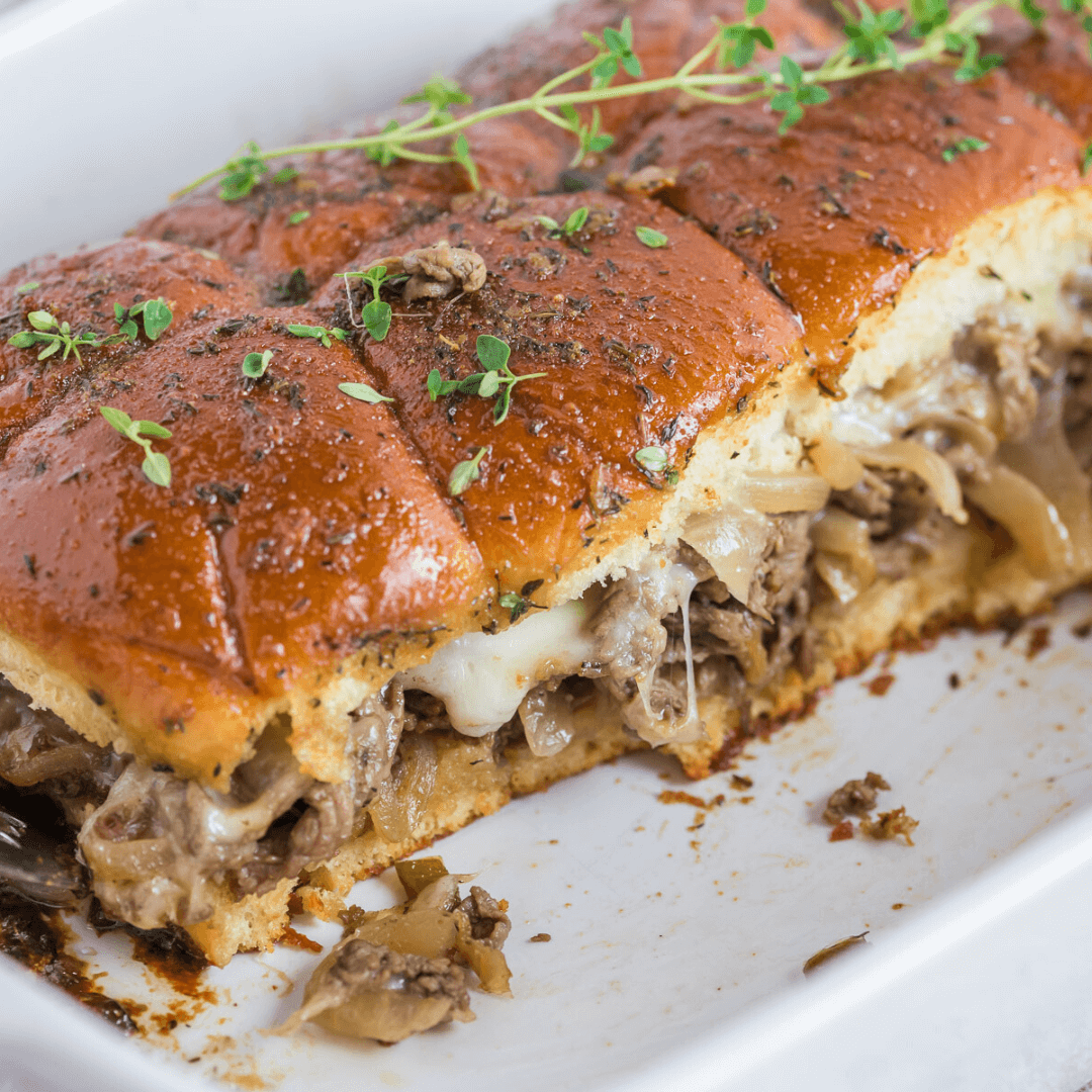 Philly cheesesteak sliders in pan with row removed revealing melty cheese, tender shaved steak and veggies.