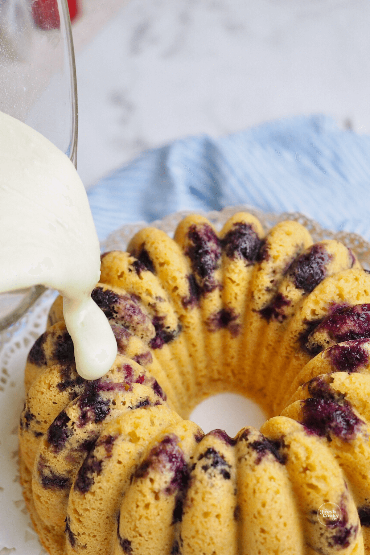 Pouring maple glaze onto cooled blueberry pancake bundt cake. 