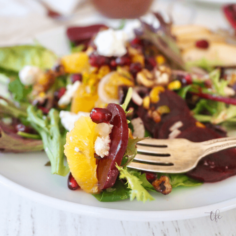 Salad bite on fork with beets, pomegranate, baby greens and orange slice.