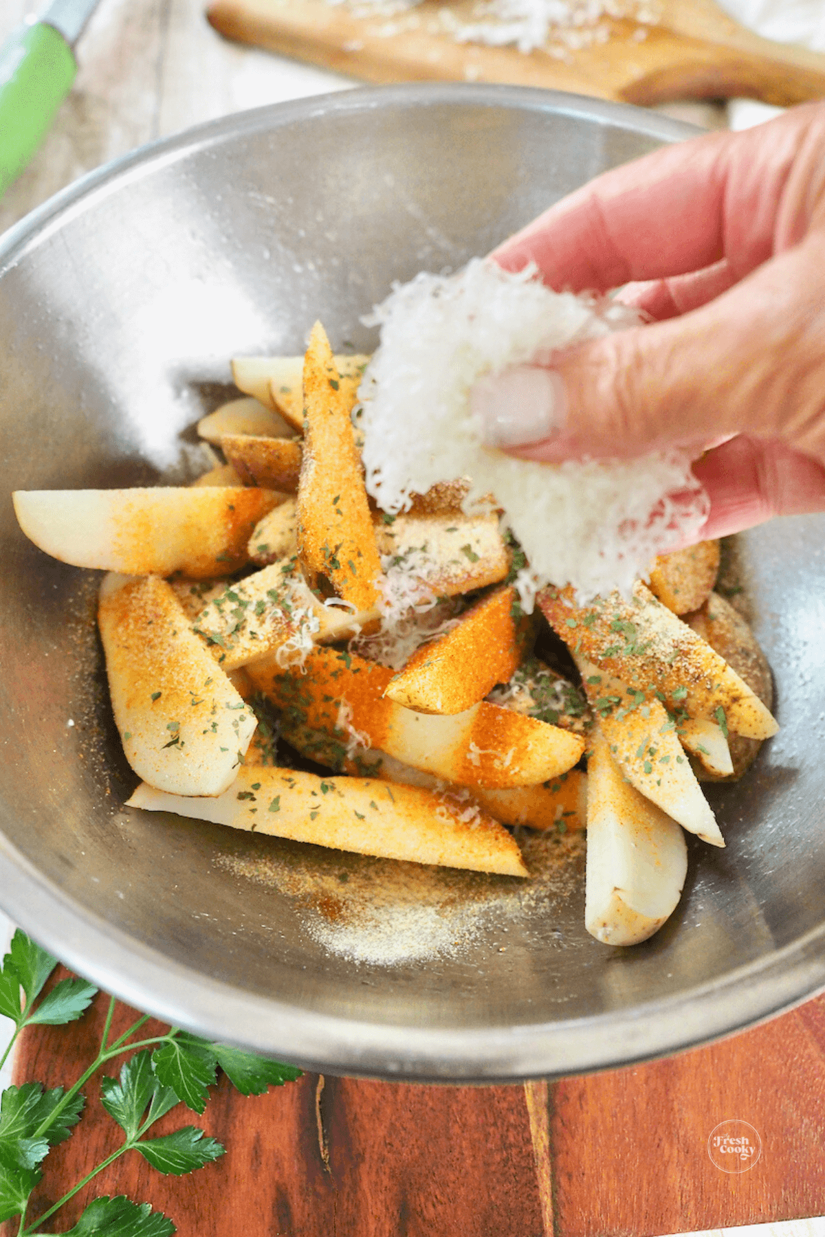 Hand adding grated parmesan cheese to seasoned fries. 