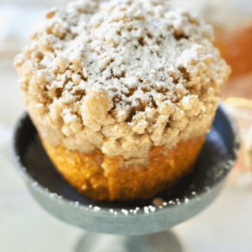 Panera pumpkin muffin on mini pedestal sprinkled with powdered sugar with generous crumb topping.