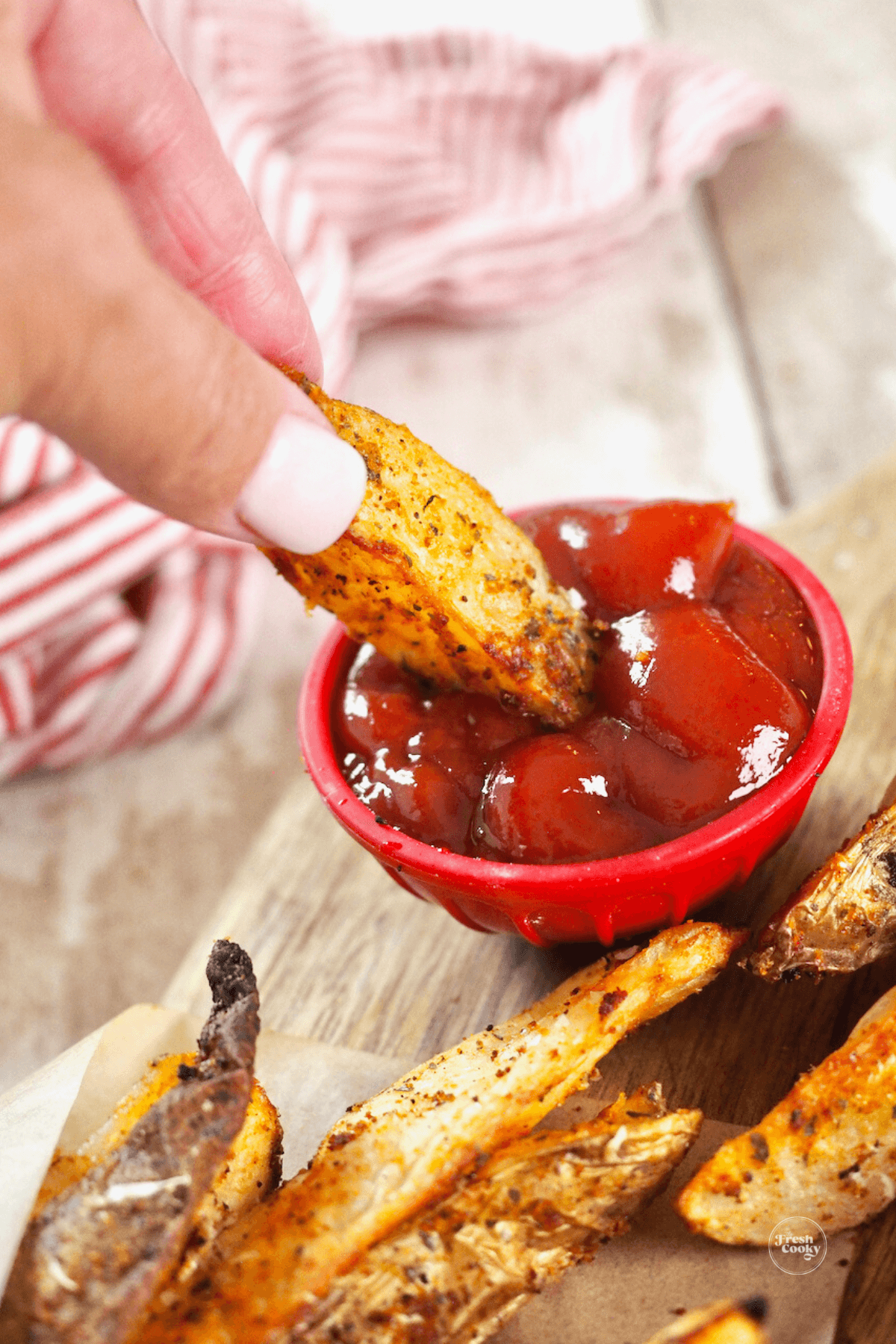 Hand dipping fry into ketchup.