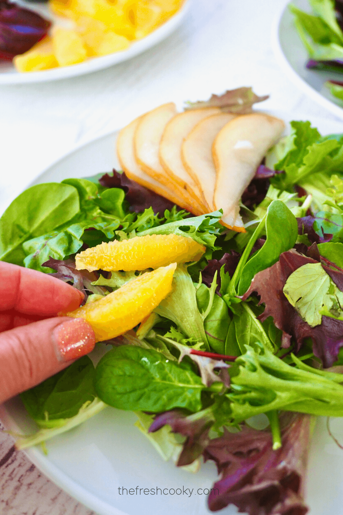 Adding slices of orange to salad greens. 