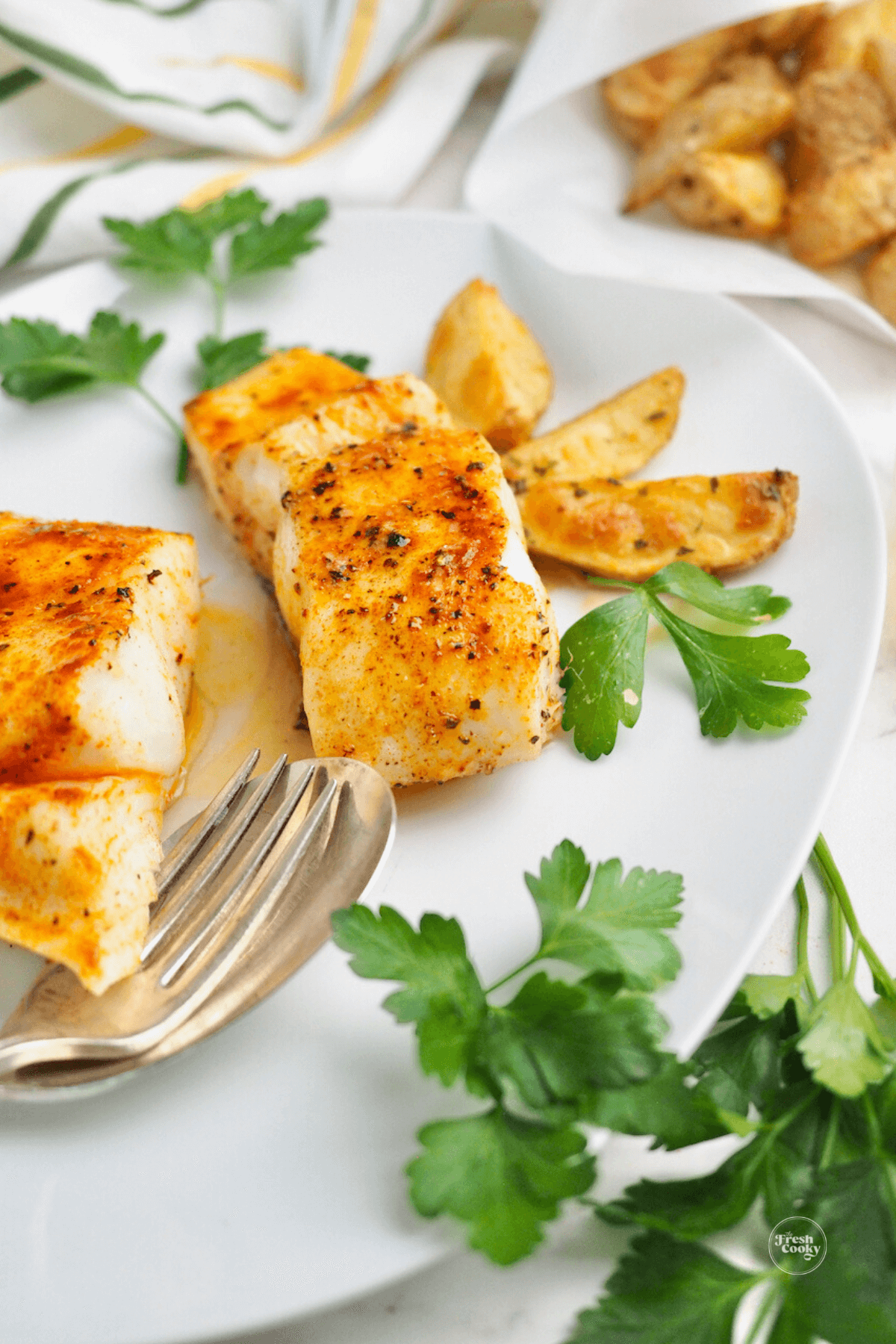 Fried halibut on pretty plate with steak fries nearby.