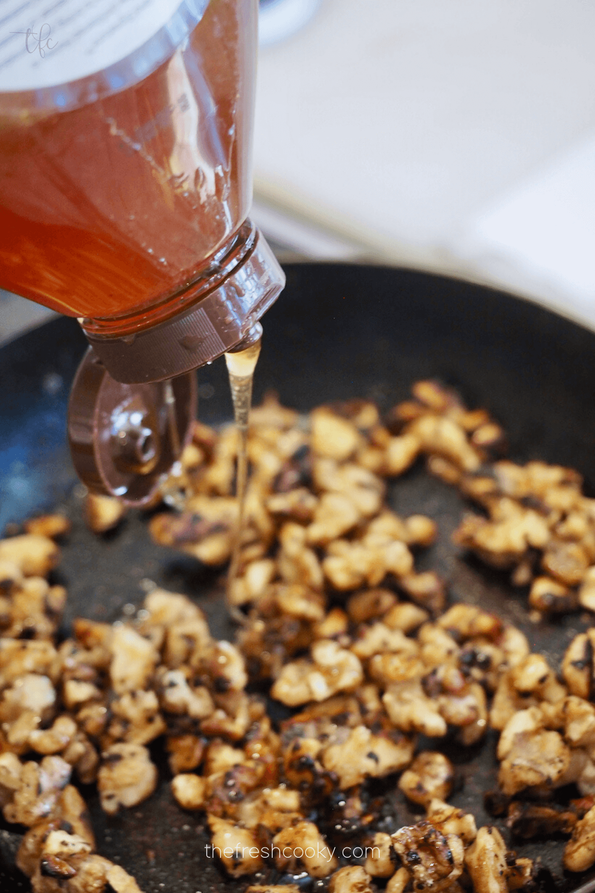 Walnuts in pan with honey drizzling in.