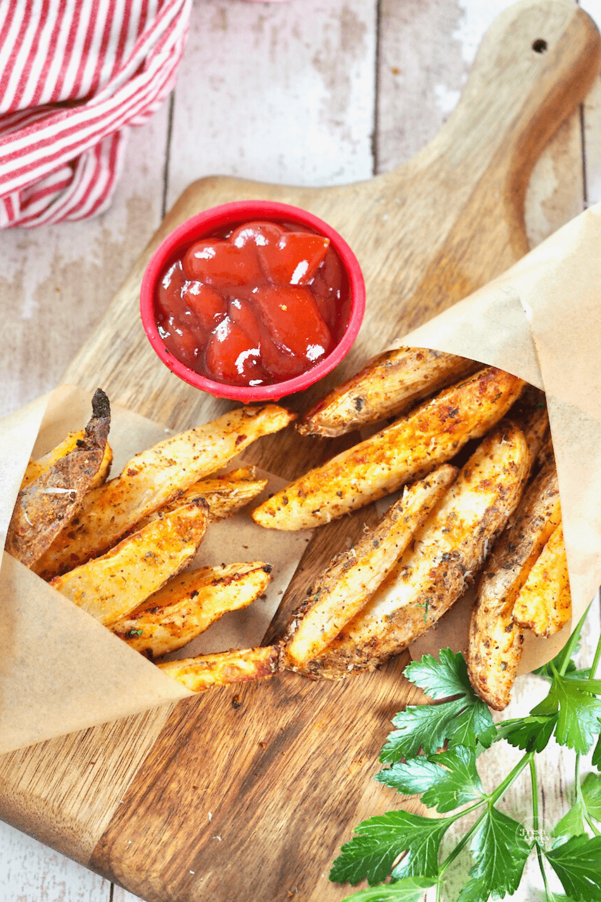 Two servings of steak fries in parchment with ketchup for dipping.