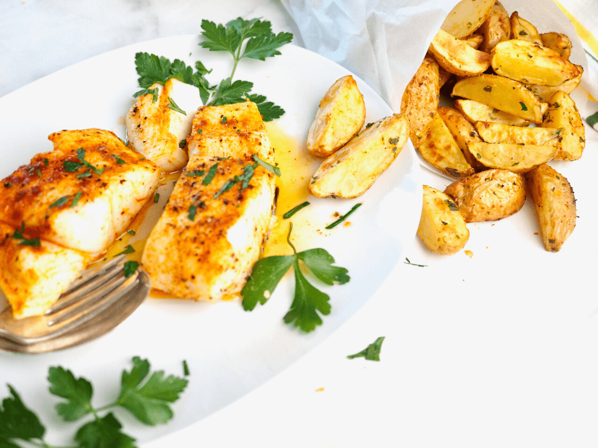 Two halibut filets on white plate with steak fries as a side.