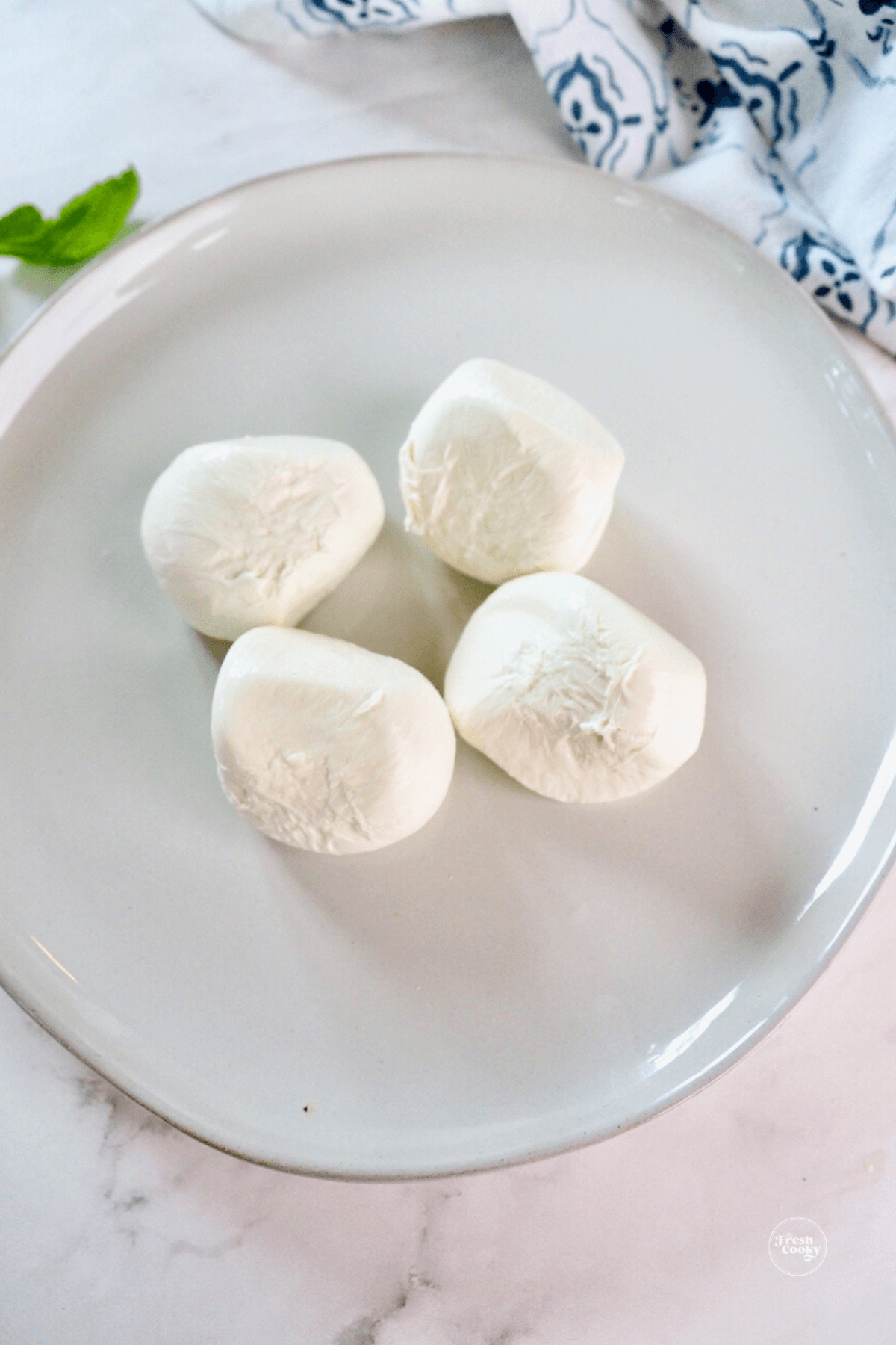 4 balls of burrata cheese on rimmed plate. 