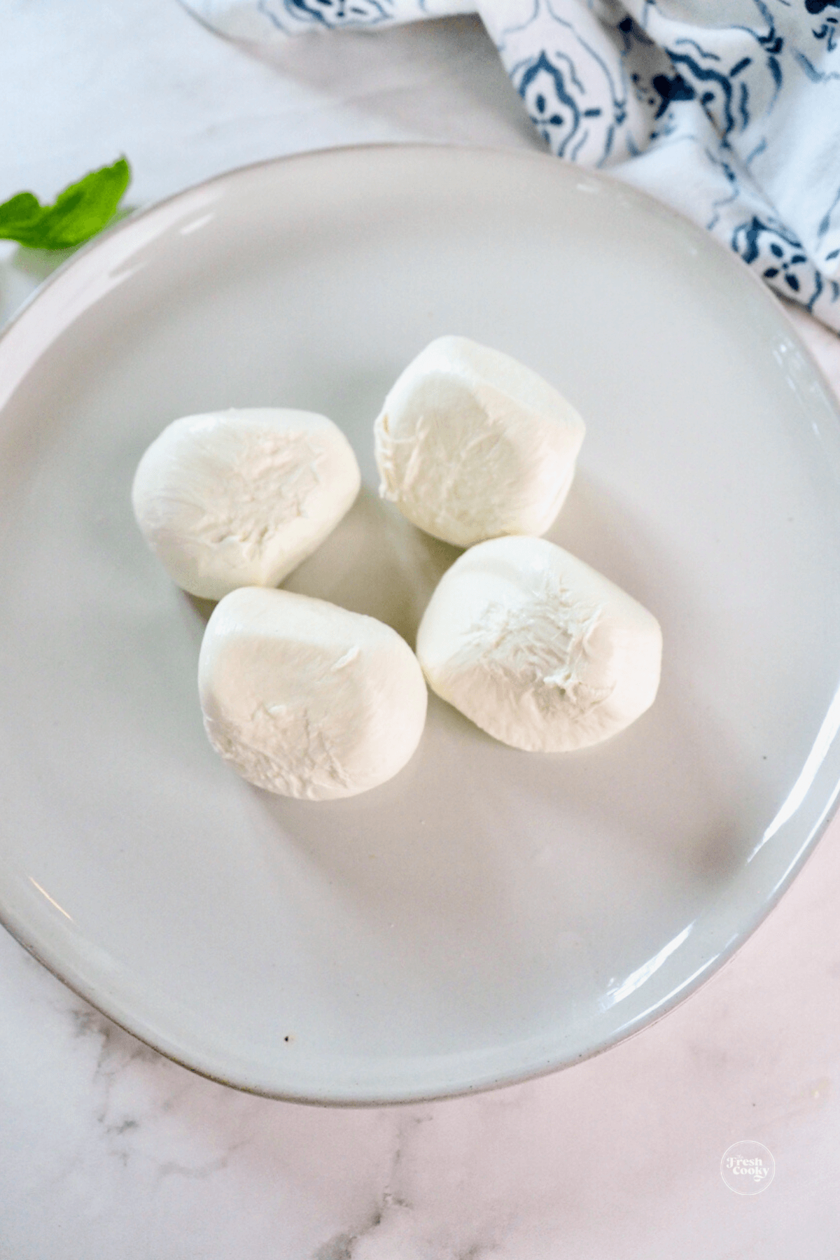 4 balls of burrata cheese on rimmed plate.