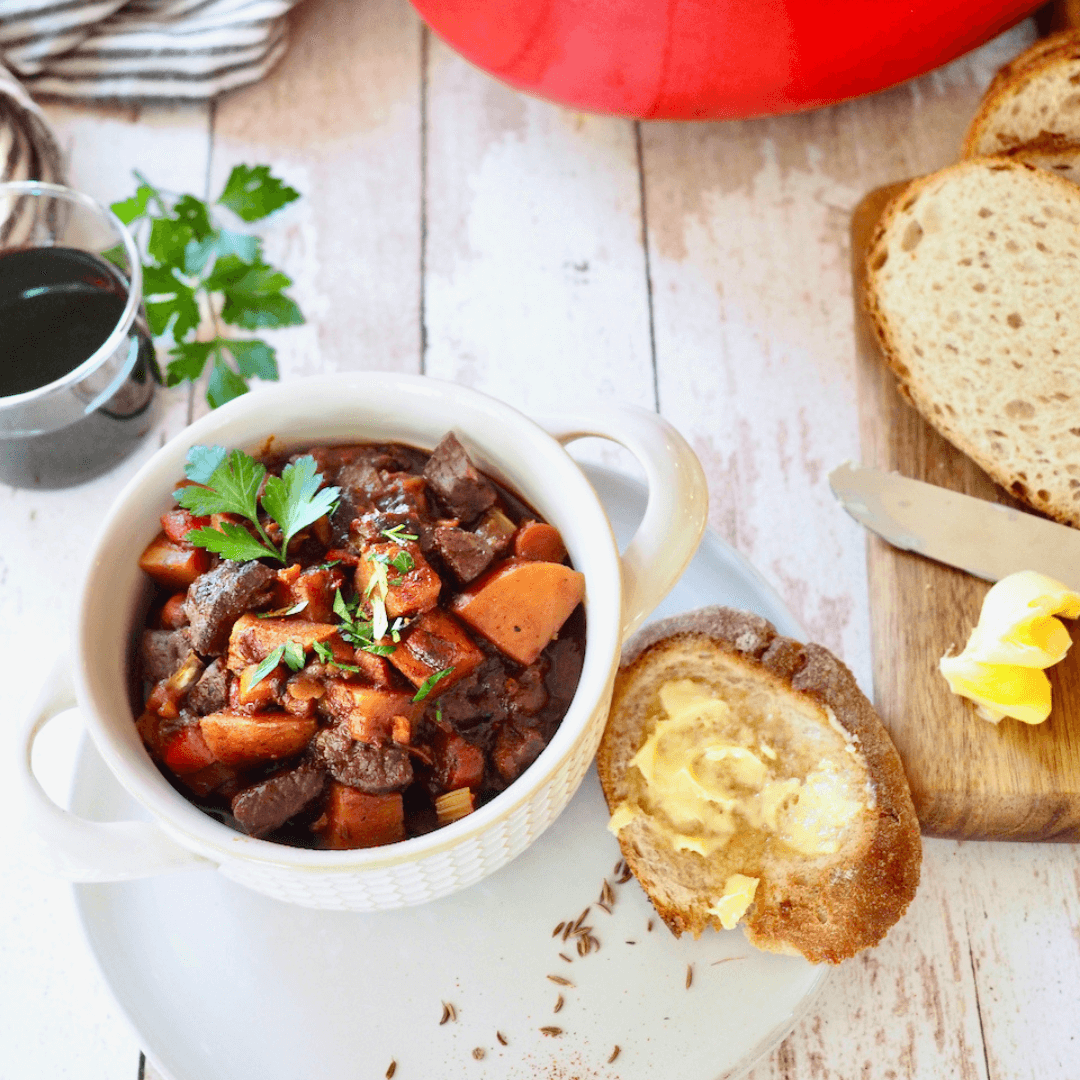 A large bowl of rich German goulash soup with rye bread.