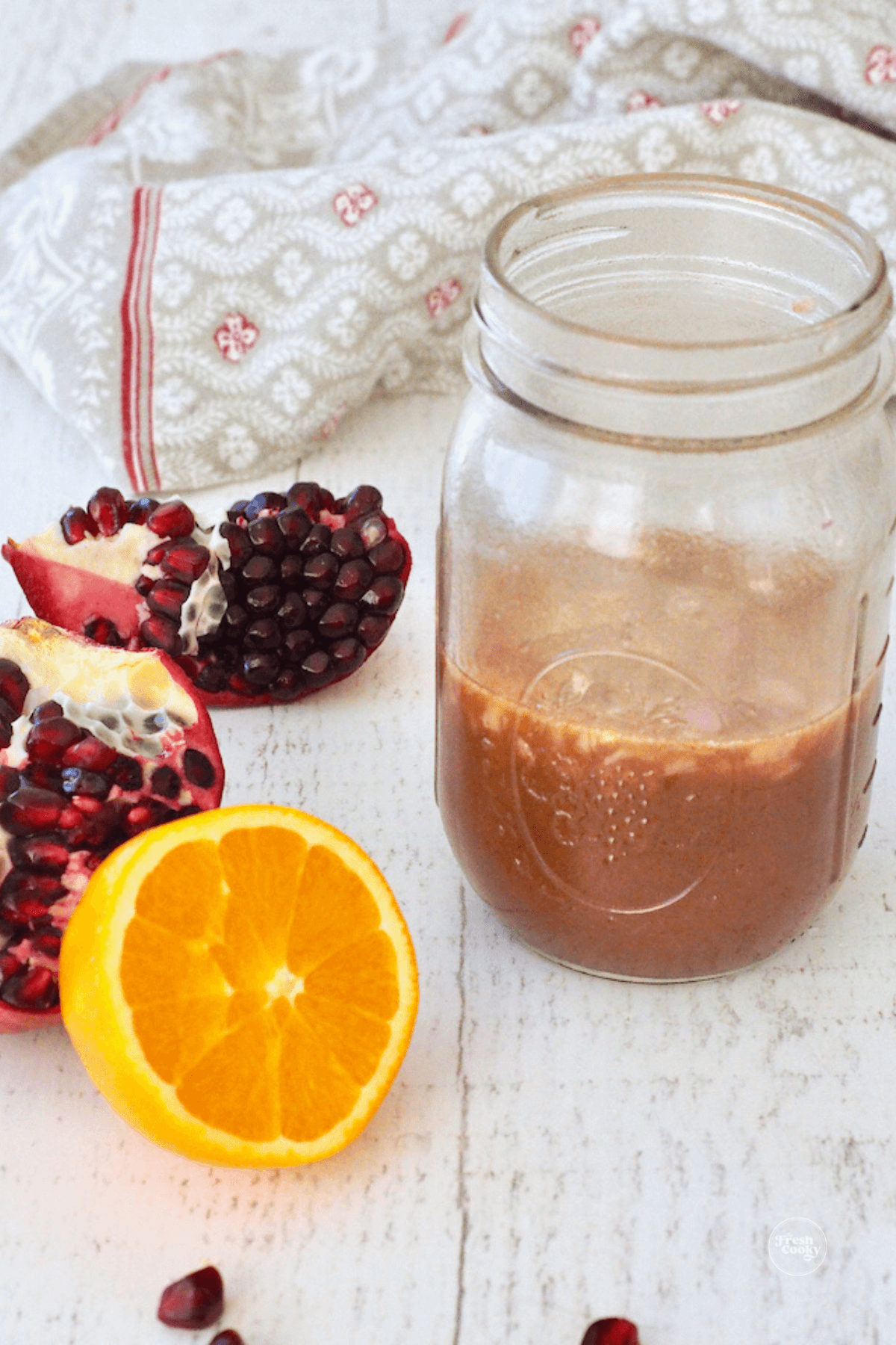 Shaken pomegranate salad dressing in mason jar with half orange and pomegranate nearby.