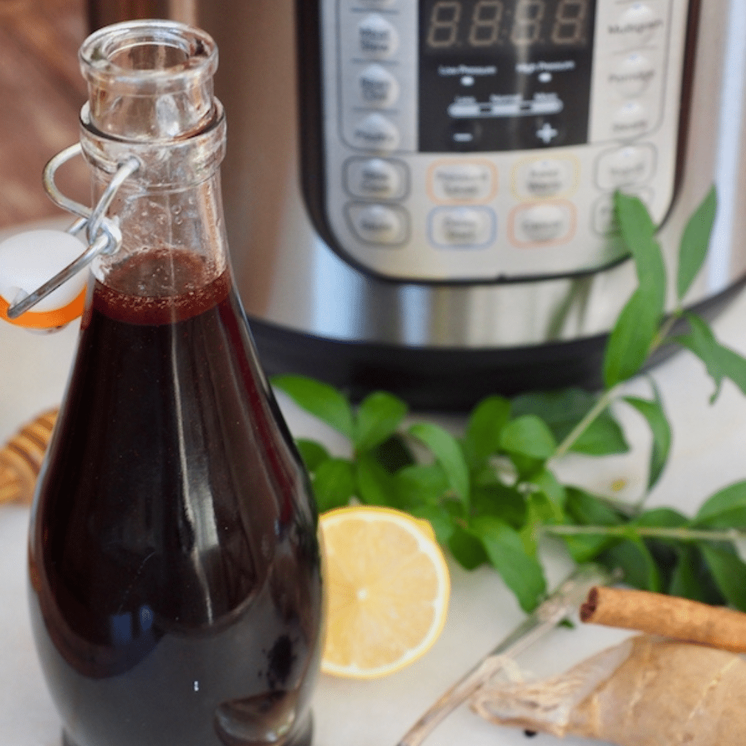 Bottle of homemade elderberry syrup in front of an instant pot.