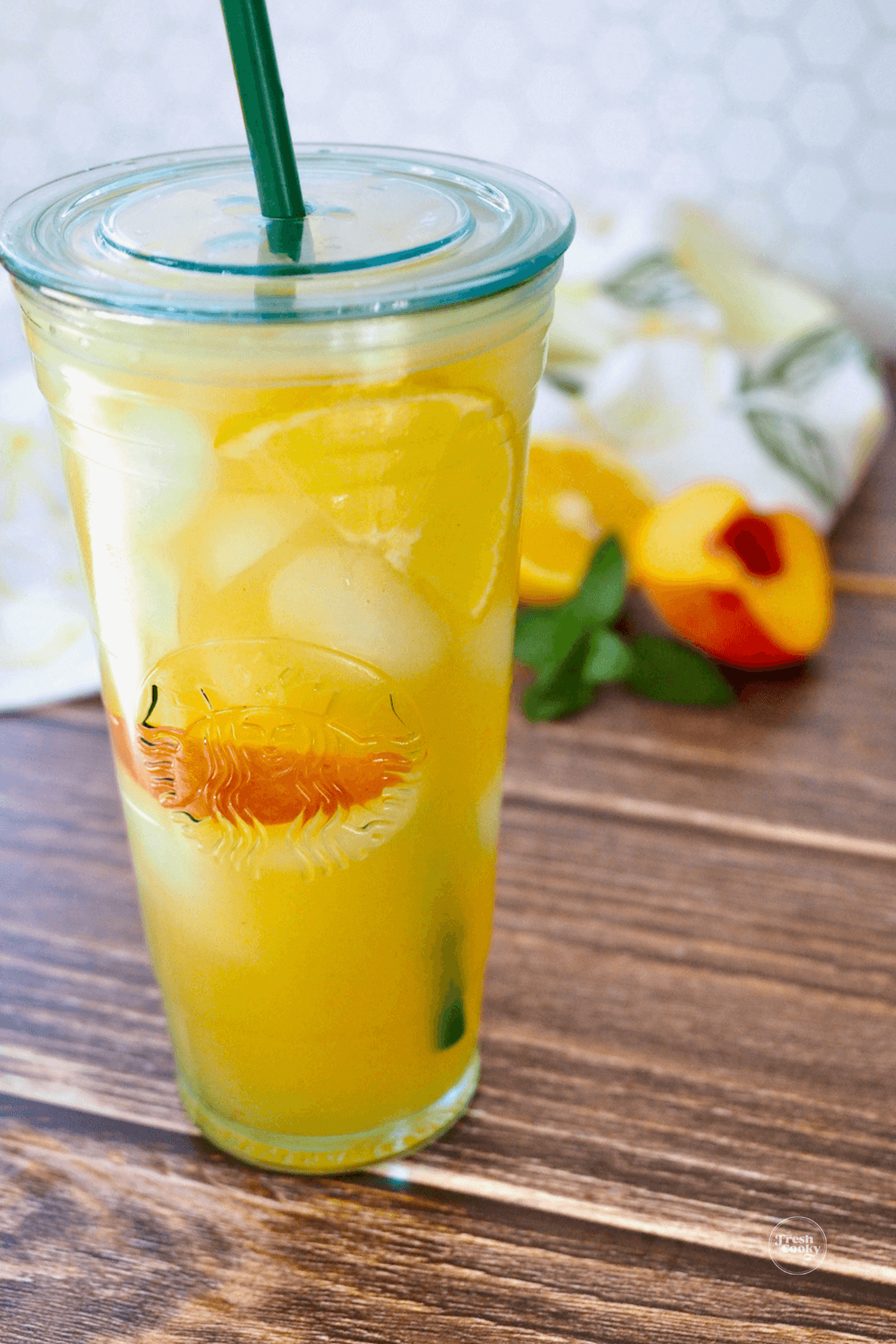 A Starbucks glass cup filled with golden-filled iced peach green tea.