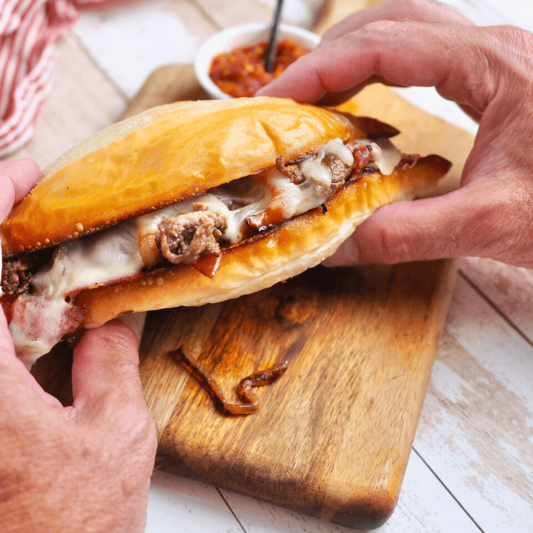 Hands holding a juicy steak bomb sandwich.