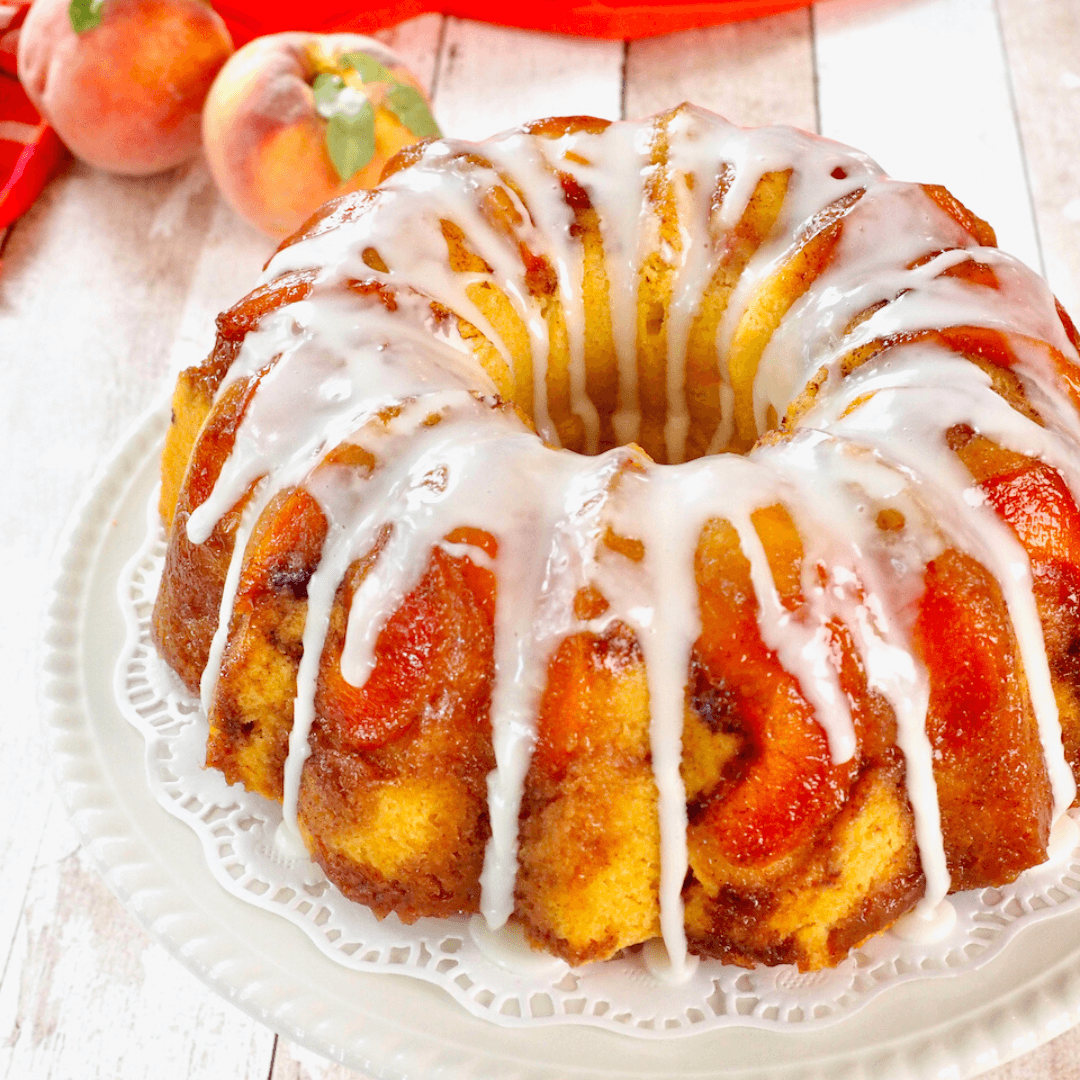 Fresh peach bundt cake on pedestal with drips of glaze.