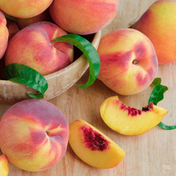 Bowl of fresh peaches with one sliced.