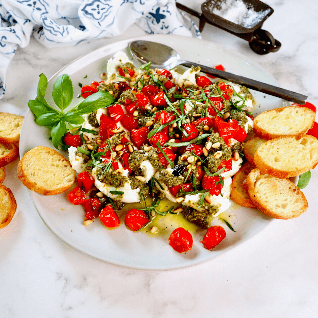 Beautiful plate with burrata pesto and roasted tomato appetizer with toasted crostini.