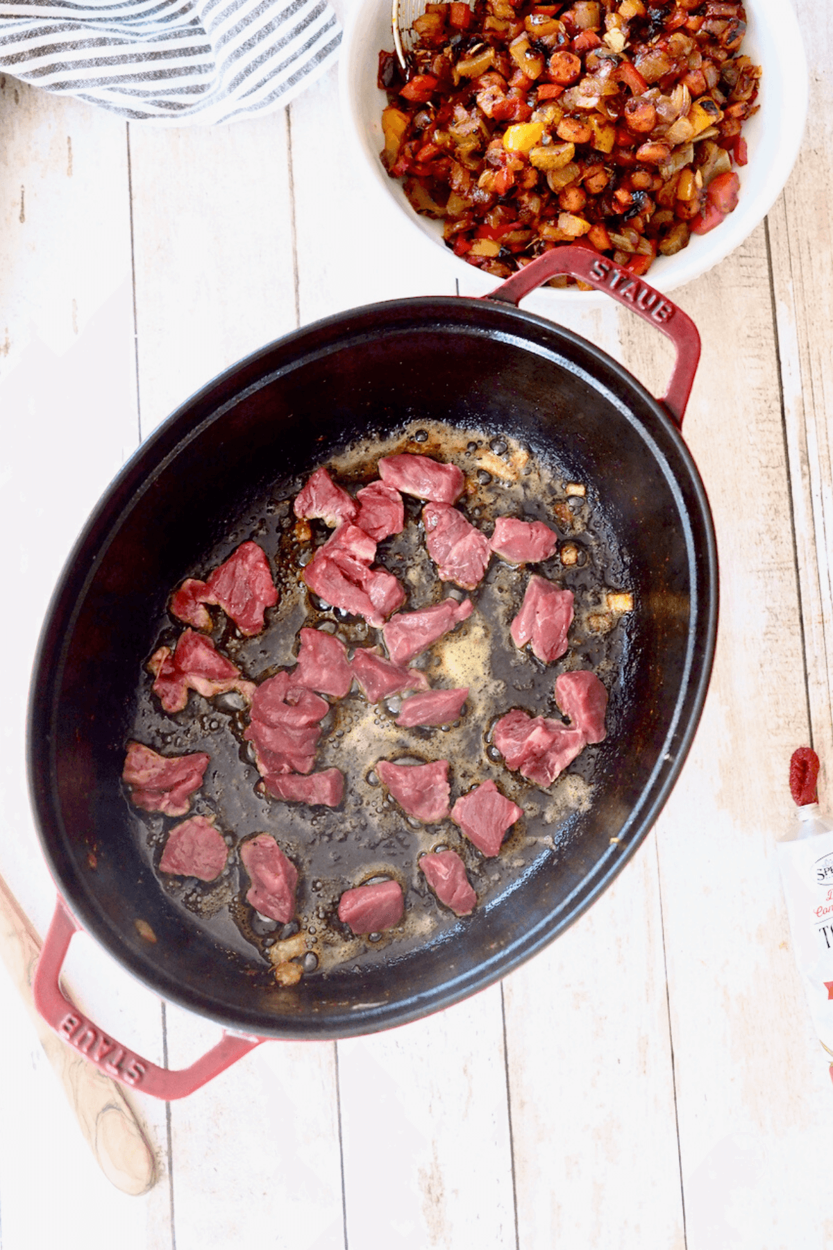 Browning beef tips in dutch oven with sauted veggies in background. 