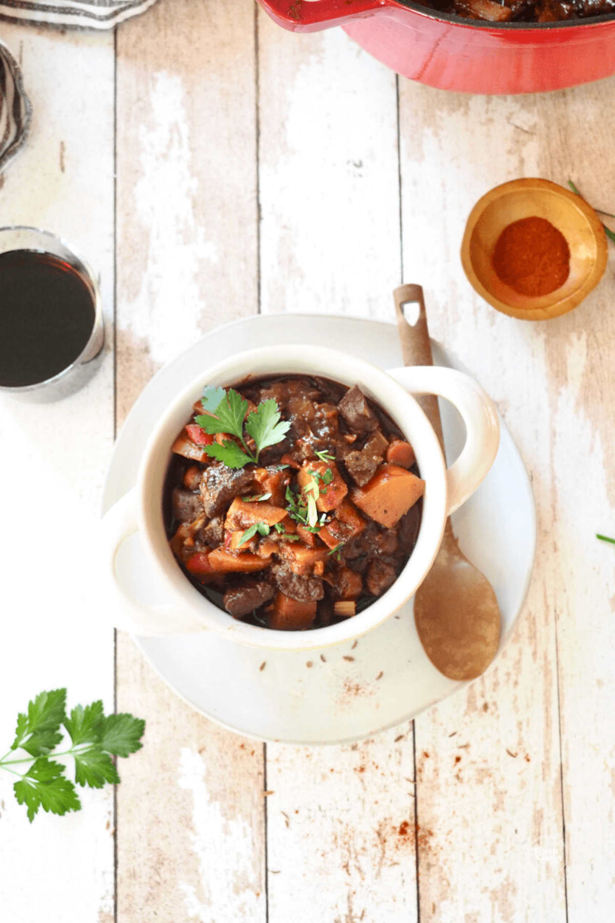 German goulash soup in double handled bowl with paprika on the side and a glass of wine.